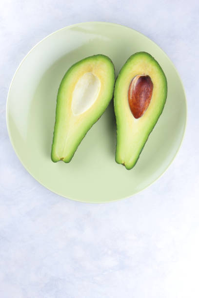 istock Avocado in a green plate on a white background, green fruit, tropical fruit, cut avocado on a marble background, healthy food, vegan, minimalism 909778862