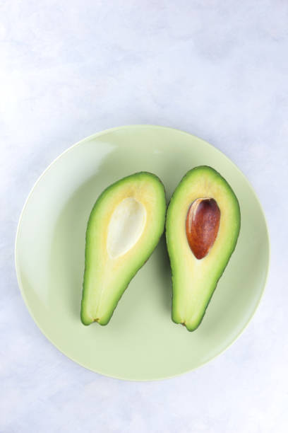 istock Avocado in a green plate on a white background, green fruit, tropical fruit, cut avocado on a marble background, healthy food, vegan, minimalism 909778898