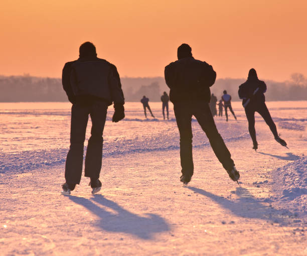 istock Ice Skaters on frozen lake at  sunset 909785338
