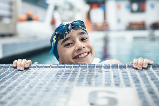 A twelve year old boy enjoys time at the swimming pool for a swim meet or lesson.  He wears a swim cap and goggles.  Healthy active lifestyle that is fun as well.