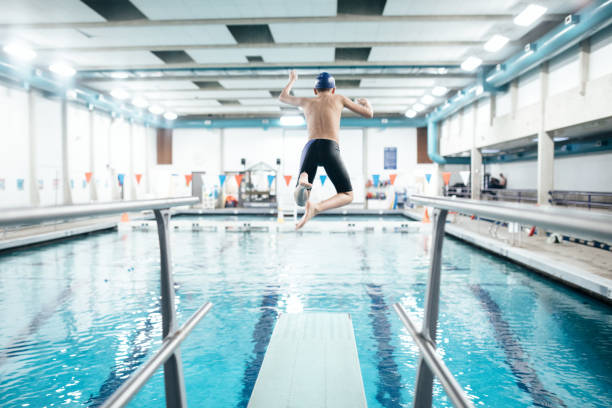 Boy In Pool on Diving Board A twelve year old boy enjoys time at the swimming pool jumping off of a diving board into the water.  Healthy active lifestyle that is fun as well. diving board stock pictures, royalty-free photos & images