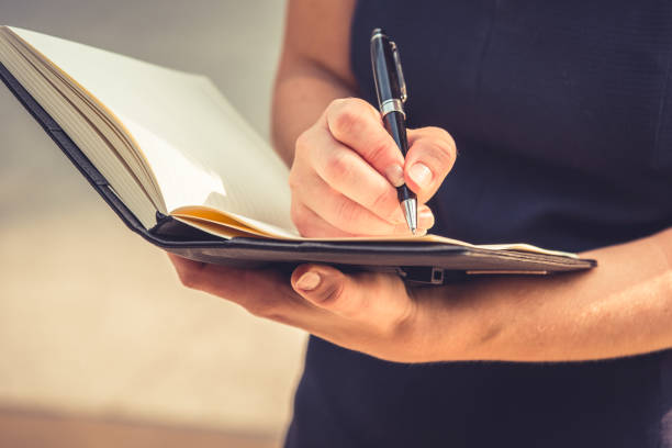 istock Close up of young woman writing down letters in notepad for making note to her diary with her hand. Business and Lifestyle concept. People and Accountant concept. Working woman theme. Warm bright 909817206