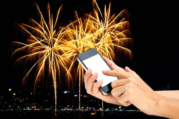 istock hand hold touch screen on smart phone or phone on fireworks on the black sky background. 909818220