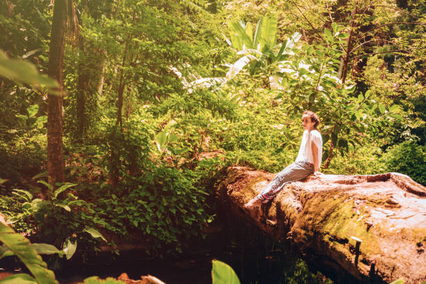 istock Young woman sitting on a fallen tree in the forest 909831970
