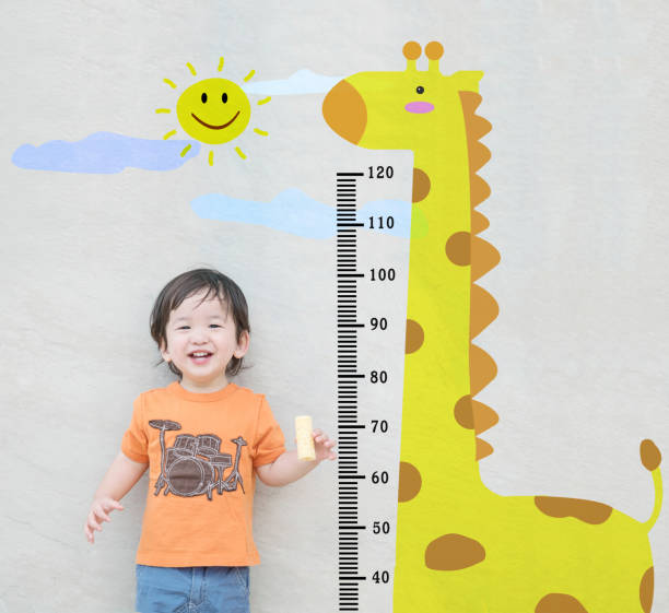 Closeup happy asian kid stand for measure height with cute cartoon at the marble stone wall textured background Closeup happy asian kid stand for measure height with cute cartoon at the marble stone wall textured background human height stock pictures, royalty-free photos & images