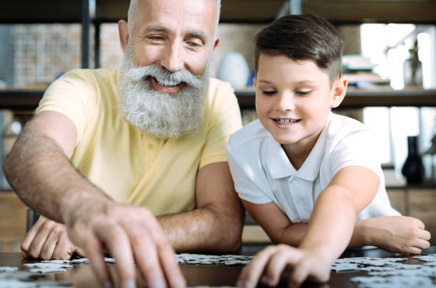 istock Kid and grandfather putting puzzle together 909847522