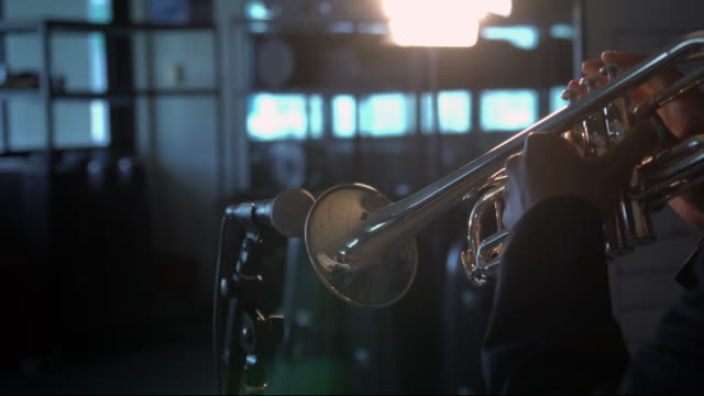 4K Footage of back side musician playing button and pushing on trumpet with microphone over the spot light in Music room background.planing from left to right
