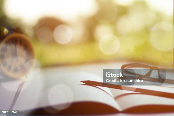 Notebook With Pencil Glasses And Clock On White Table With Yellow Light Background And Beautiful Bokeh Selective Focus Vintage Style Stock Photo - Download Image Now