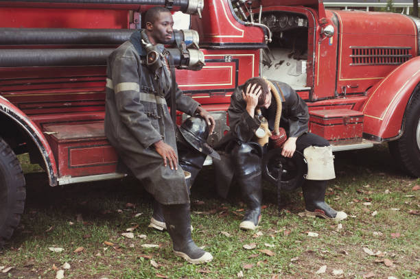 Multi-Ethnic Firemen sitting on fire truck tired and sad. It is antiquity equipment and truck.Can be use for brief Accident also. Photo was taken during suttonalypse in Quebec Canada.