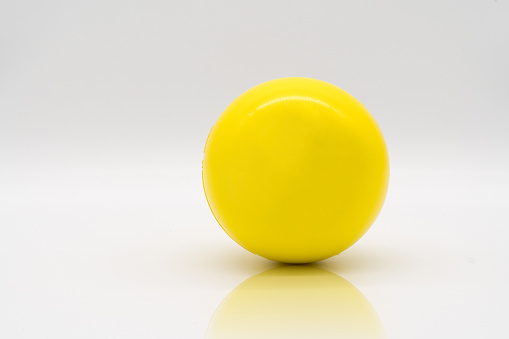 Yellow stress ball rolling on reflection floor isolated on white background.