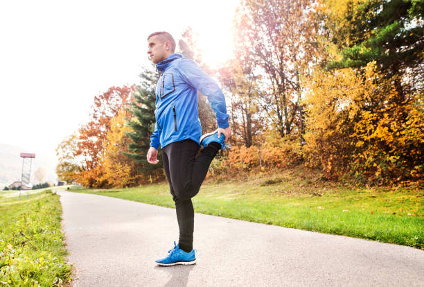 istock Young runner in autumn park standing on concrete path. 909878550