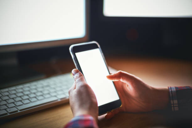 Male hands using phone with two PCs working in background