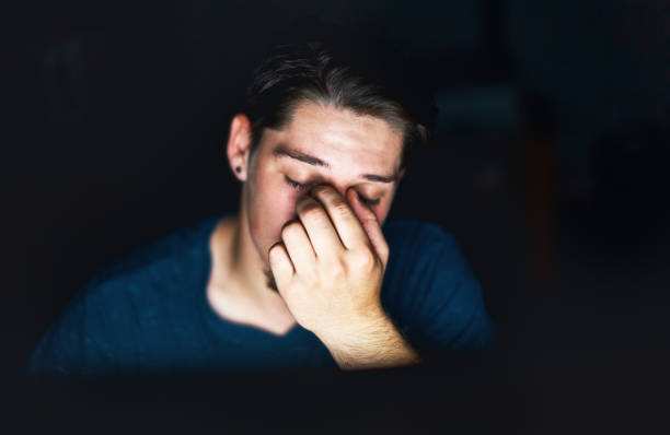 istock Tired young man working late lit by computer rubs eyes 909882638