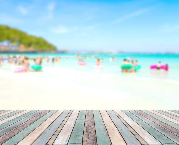 istock Wood table top with blurred people at the beach 909886116
