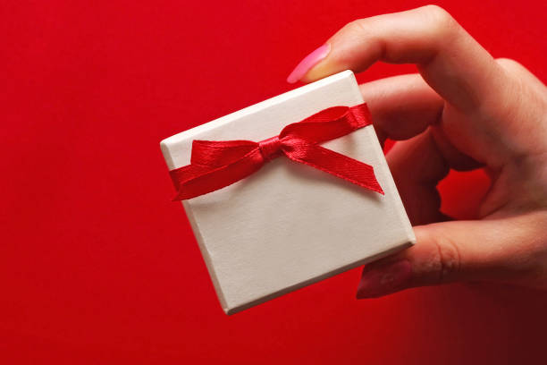 istock A girl is holding a gift box with a bow on a red background. 909886468