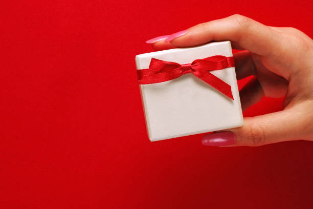 istock A girl is holding a gift box with a bow on a red background. 909886474