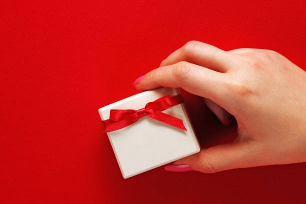 istock A girl is holding a gift box with a bow on a red background. 909886476