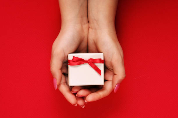 istock A girl is holding a gift box with a bow on a red background. 909886478