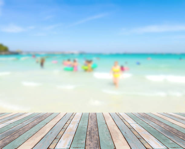 istock Wood table top with blurred people at the beach 909886652