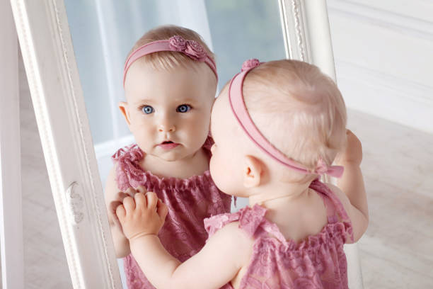Little pretty girl plays with a big mirror. Portrait of the little girl with reflection in a mirror stock photo
