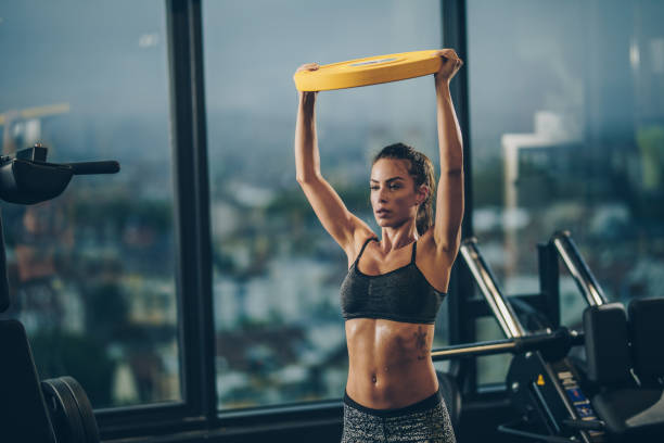 muscular construir mulher tendo treinamento cruzado em uma academia, durante o exercício com disco de peso. - sports training muscular build women body care - fotografias e filmes do acervo