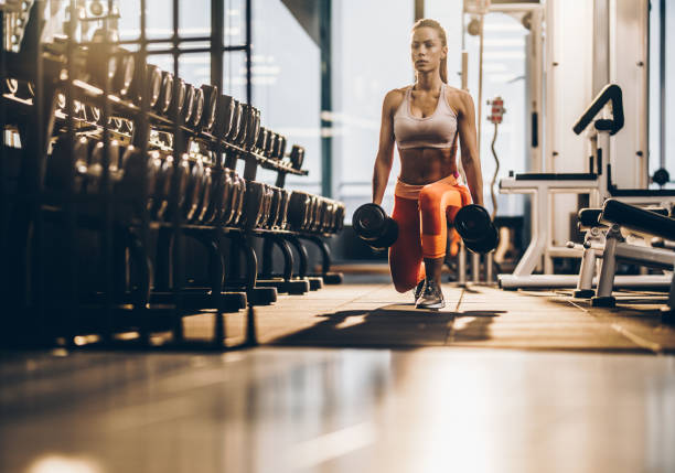 sportlerin mit hanteln in der longe lage im fitnessraum trainieren. - ausfallschritt stock-fotos und bilder