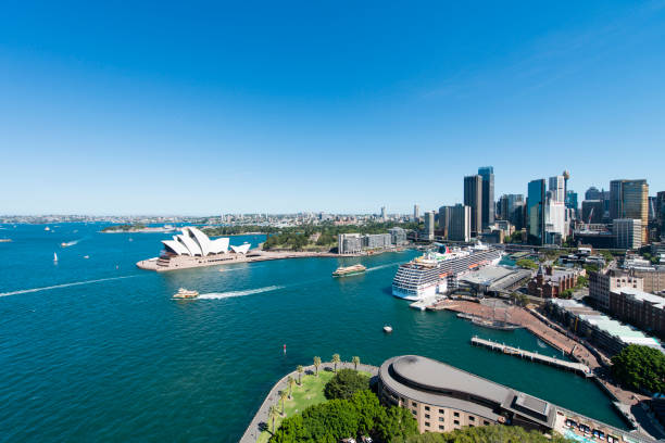 The Sydney Opera House seen from the Harbor Bridge during a hot summer day. In the back the skyscrapers of downtown Sydney.