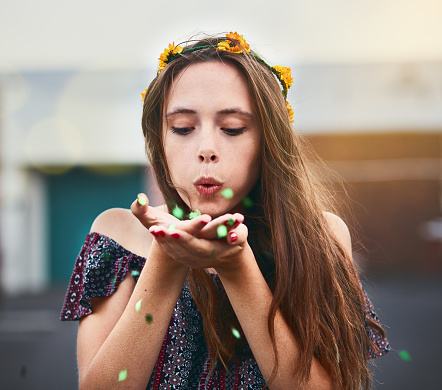 A pretty teenager wearing a floral coronet, perhaps a bridesmaid, blows multicoloured confetti from her hands.