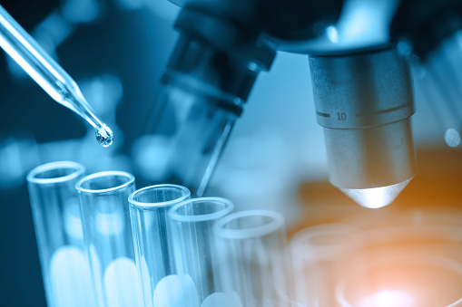 Midsection of young female biochemist using pipette over multi well plate at laboratory