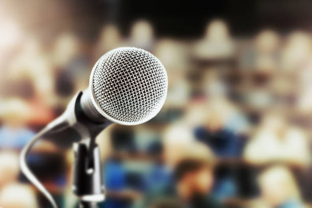 istock Shiny vocal microphone with defocussed  audience in background 909911814