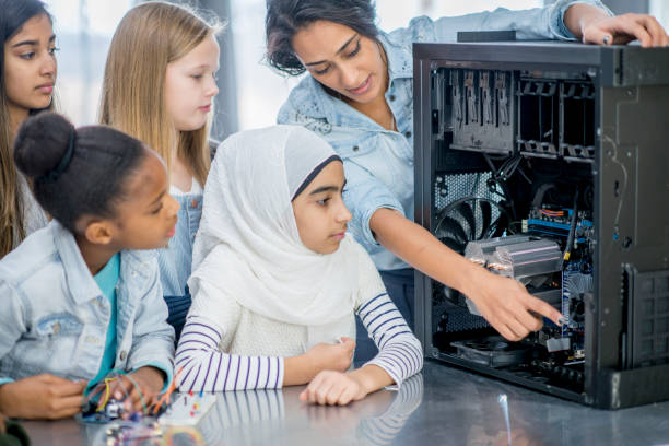 Looking Inside A Computer A group of elementary school children and their teacher and indoors in their classroom. The teacher has opened a desktop computer to view the inside components. She is pointing to certain parts and explaining what they do. stem topic stock pictures, royalty-free photos & images