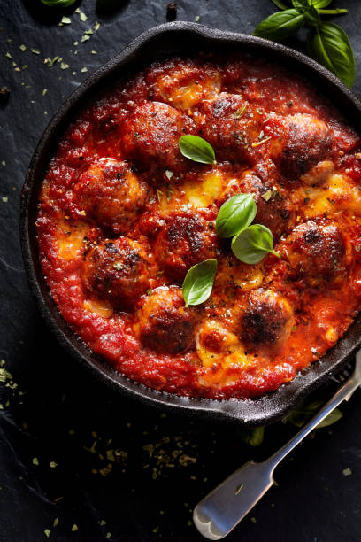 istock Meatballs in tomato sauce with addition cheese and fresh basil on iron pan 909920638