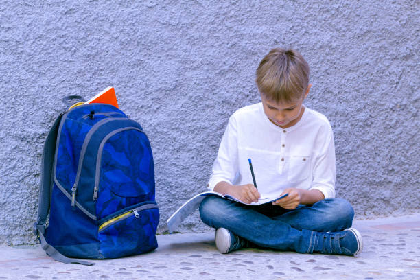 istock Boy doing school homework. Kid reading, writing and thinking sitting on the ground. 909923354