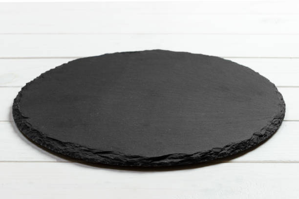 istock Black slate round stone on wooden background, top view, copy space 909927176