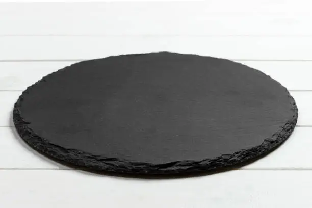 Photo of Black slate round stone on wooden background, top view, copy space