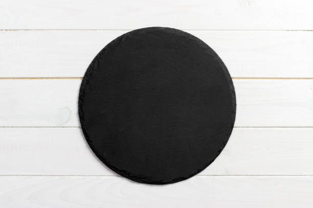 istock Black slate round stone on wooden background, top view, copy space 909927180