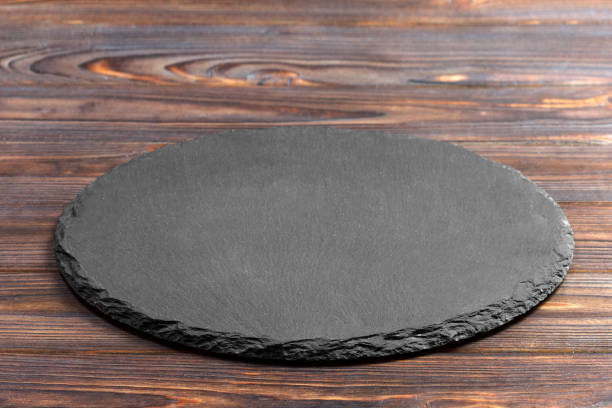 istock Slate plate on table. black slate stone on wooden background. copy space 909927352