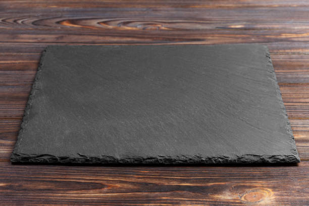 istock black slate stone on wooden background. copy space 909927354