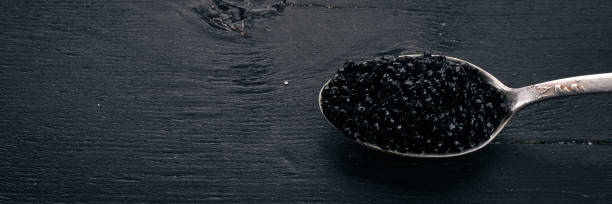 istock Spoon with black caviar on a wooden background. Top view. Free space for text. 909930658