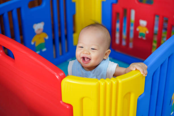 Cute asian 9 months old baby boy playing in colorful plastic playpen, Adorable child having fun indoor, Little smiling kid standing in crib stock photo
