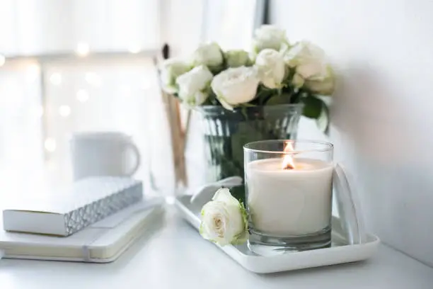Photo of White room interior decor with burning hand-made candle and bouq