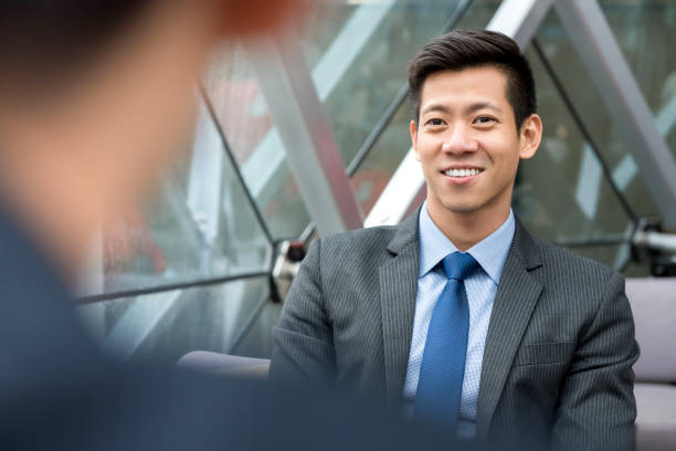Asian businessman sitting at office lounge Handsome Asian businessman sitting at office lounge talking with his colleague office buddies stock pictures, royalty-free photos & images