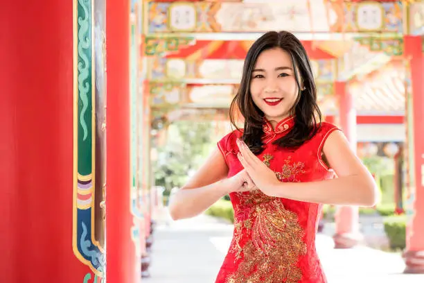 Smiling Asian woman in traditional red cheongsam qipao dress making salute