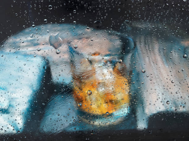 Whiskey glass between wooden boards behind wet window glass