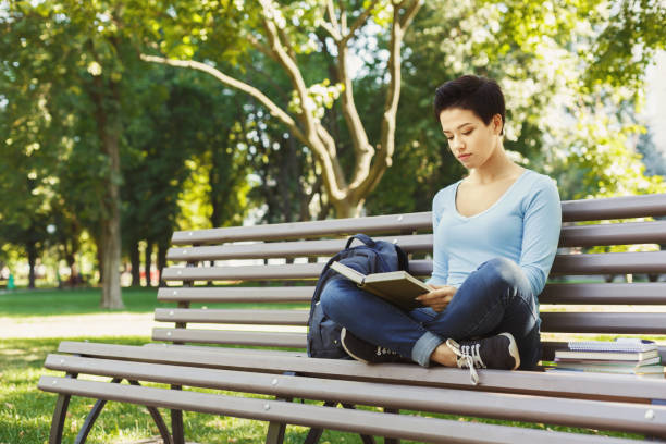 istock Young woman reading book in university campus 909938784