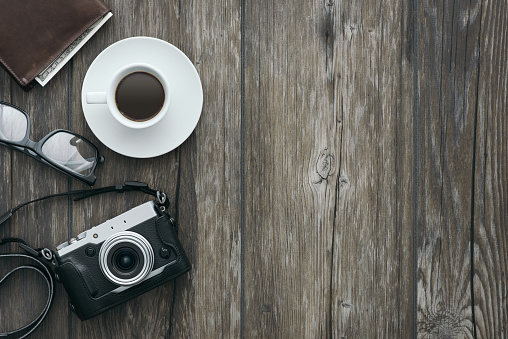 Vintage professional camera on a wooden desktop with a wallet, glasses and a coffee, hipster style