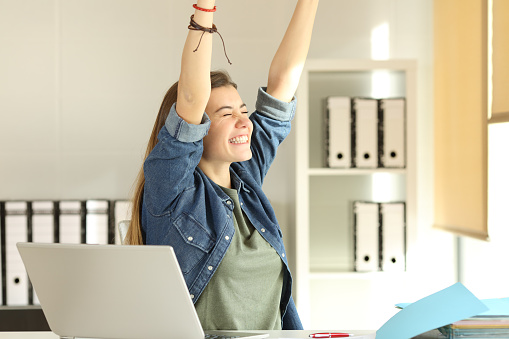 Portrait of a young satisfied intern raising arms at office