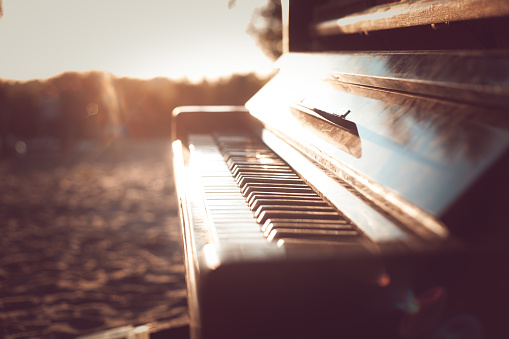 vintage piano standing on the beach on sunset background