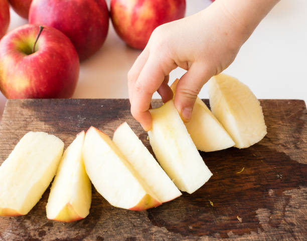 istock Cropped Hand Of Child Holding Apple On Cutting Board 909965042