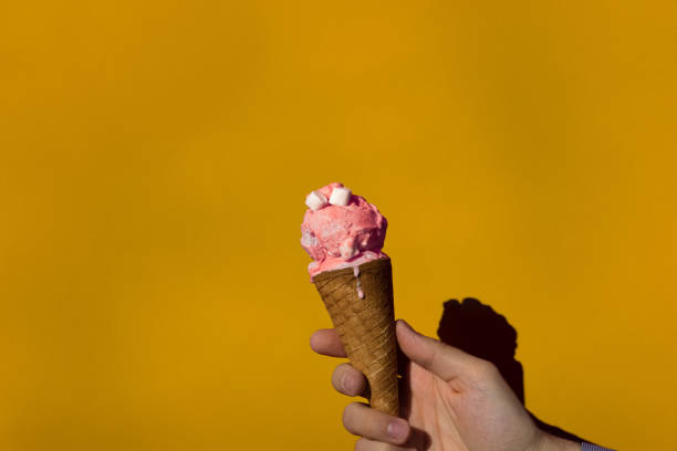 istock Cropped Hand Holding Ice Cream Against Yellow Wall On Sunny Day 909965666